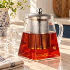Square glass teapot brewing a ruby herbal infusion on a kitchen counter