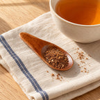 Small wooden tea spoon holding a herbal blend beside a cup of tea